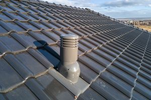 A close-up of a roof vent installed on a modern tile roof, showcasing the importance of enhancing roof ventilation for improved airflow and moisture contro