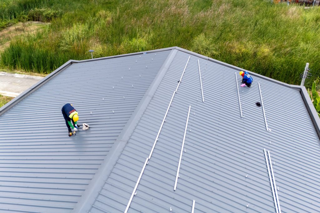 aerial-view-of-two-workers-installing-solar-panel-mounting-rails-on-gray-metal-roof